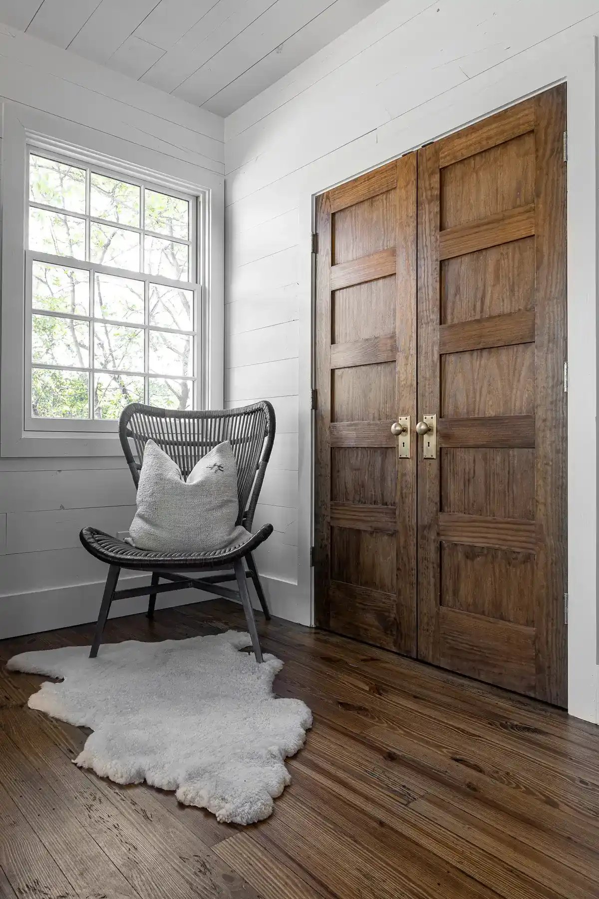 Cozy corner with a rustic wooden door, wicker chair, sheepskin rug, and shiplap walls.