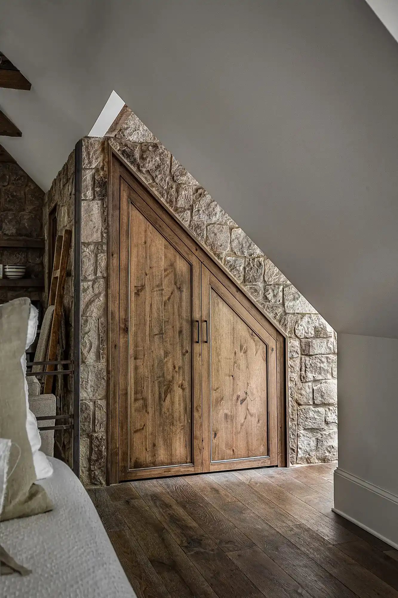 Attic bedroom with custom wooden storage doors set into a stone wall, complementing the hardwood floors.