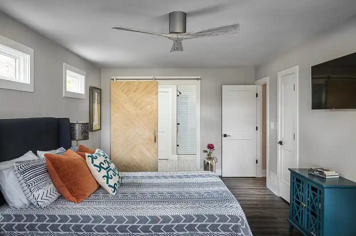 Modern bedroom with patterned bedding, chevron wood flooring, and sliding barn door.