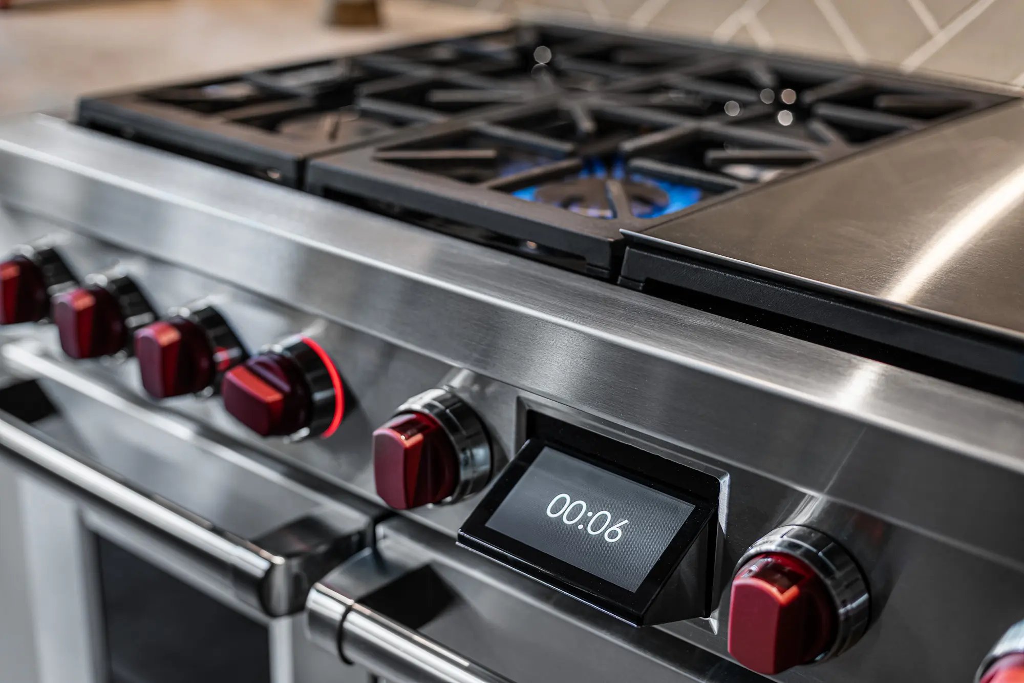  Close-up of a stainless steel gas stove with red control knobs and digital timer display, showcasing modern kitchen appliances.