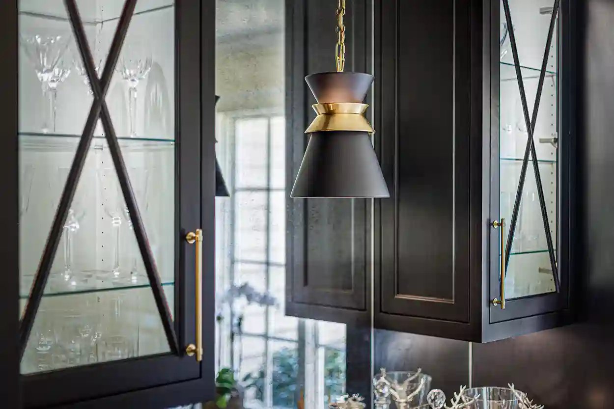 Chic pendant light above dark cabinetry with glassware display in a modern kitchen.