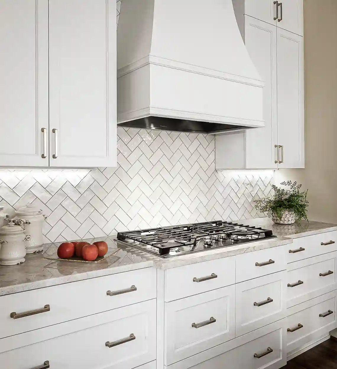 Elegant white kitchen with herringbone backsplash and stainless steel gas stove.