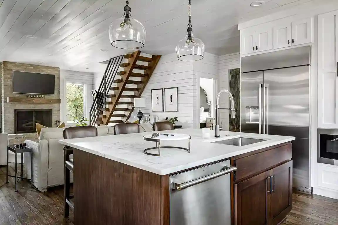 Modern rustic kitchen featuring a marble-topped island, stainless steel appliances, and chic pendant lighting with a cozy living area in the background.