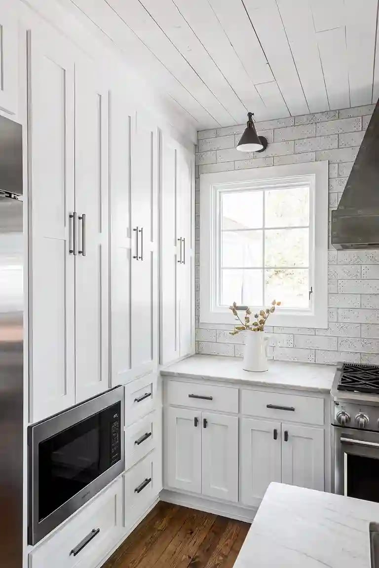 Elegant white kitchen cabinetry with marble countertops, subway tile backsplash, and a single pendant light, embodying a clean and bright aesthetic.