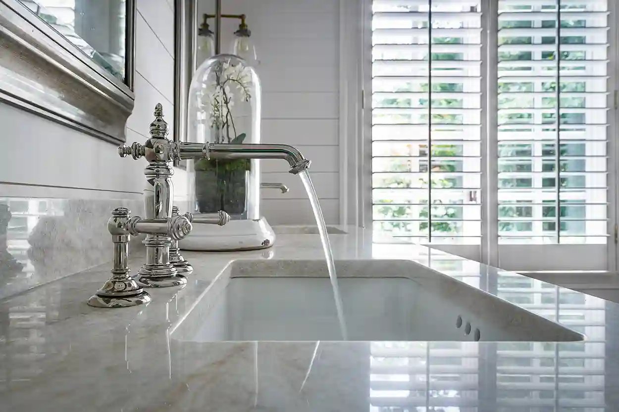 Luxurious kitchen sink with classic silver faucet, marble countertop, and a view to greenery through white shutters