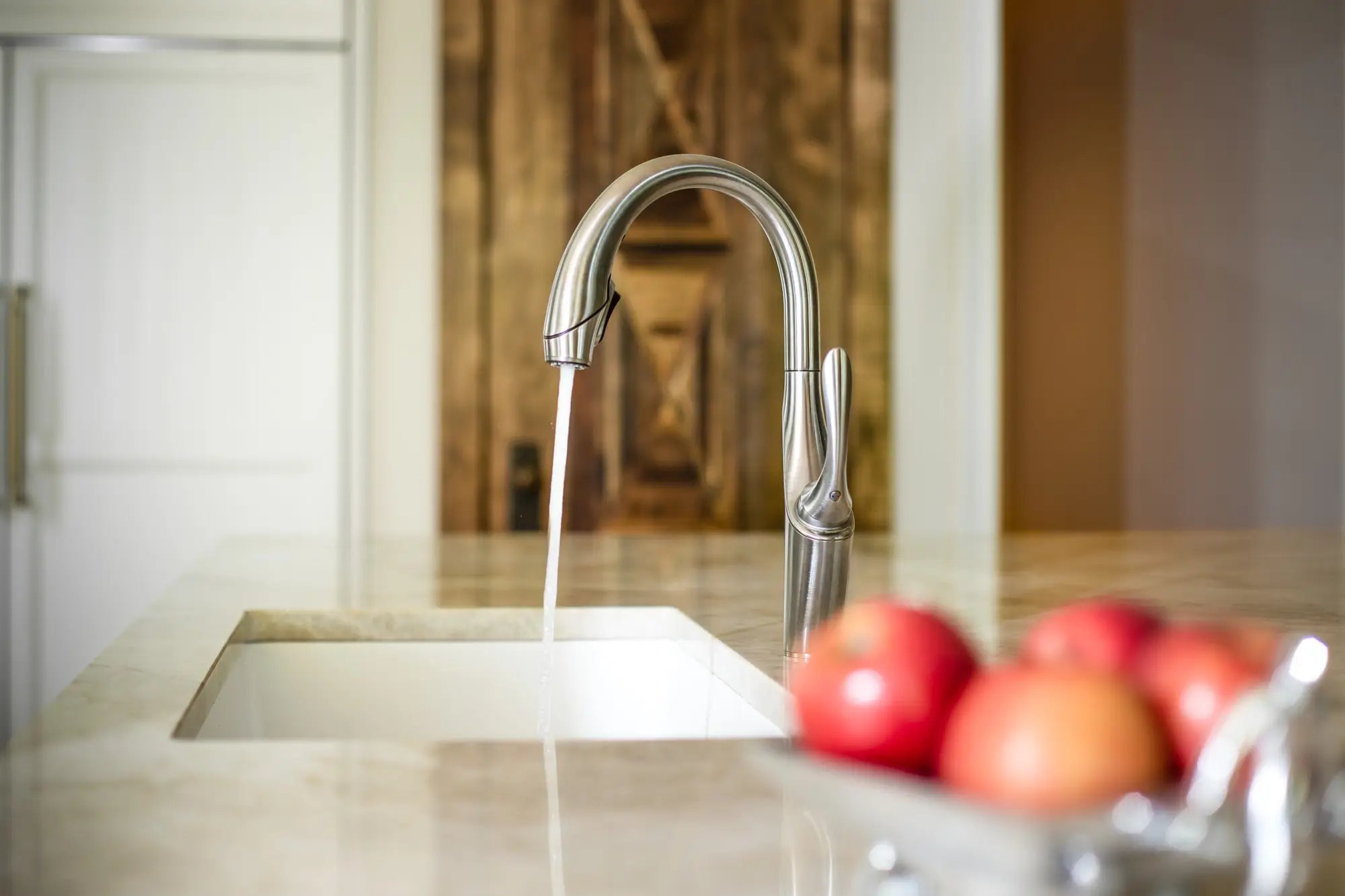  Modern kitchen faucet running water over sink with a blurred background of fresh apples and cabinetry.
