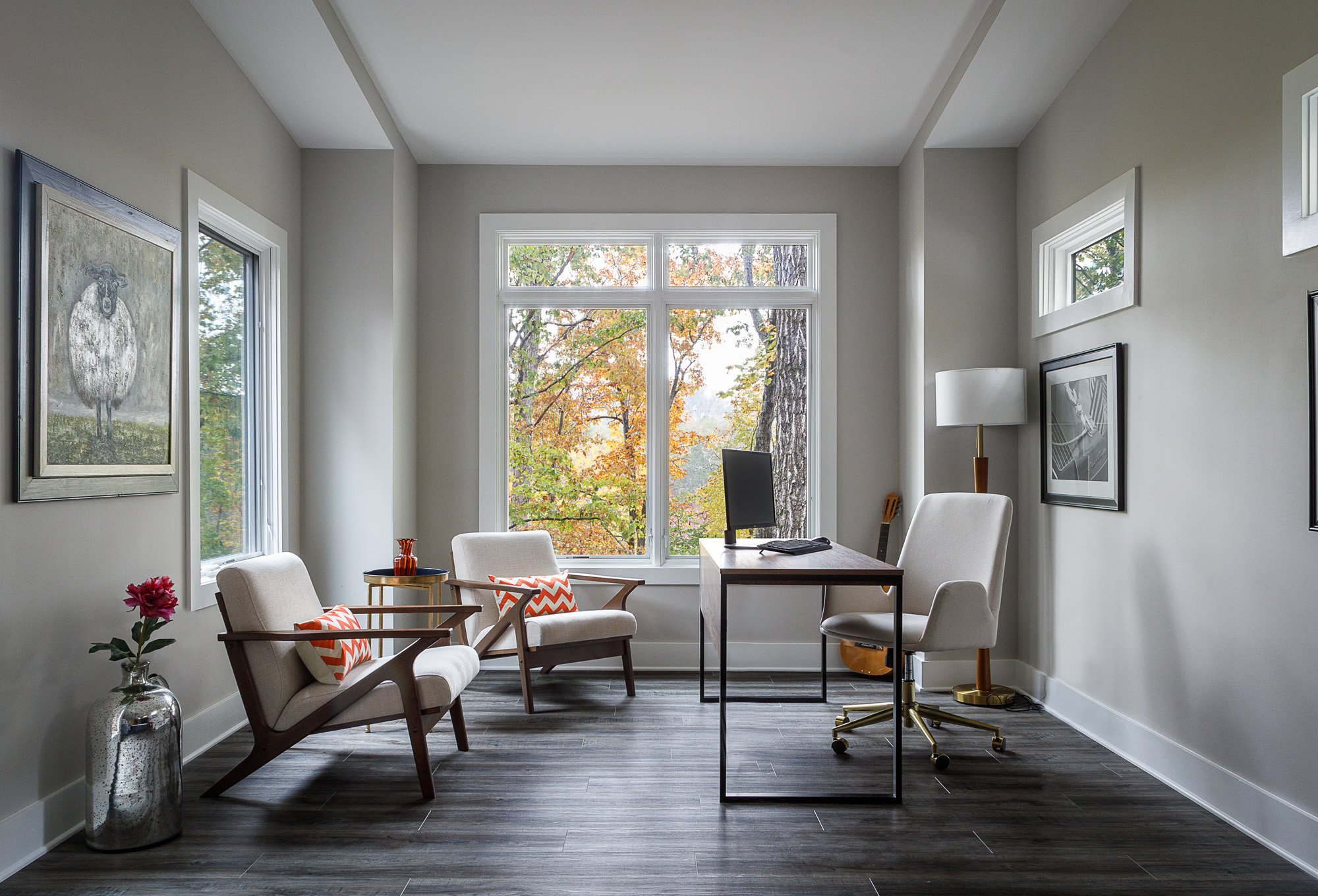 Elegant home office with large windows, modern furnishings, and autumnal forest view.