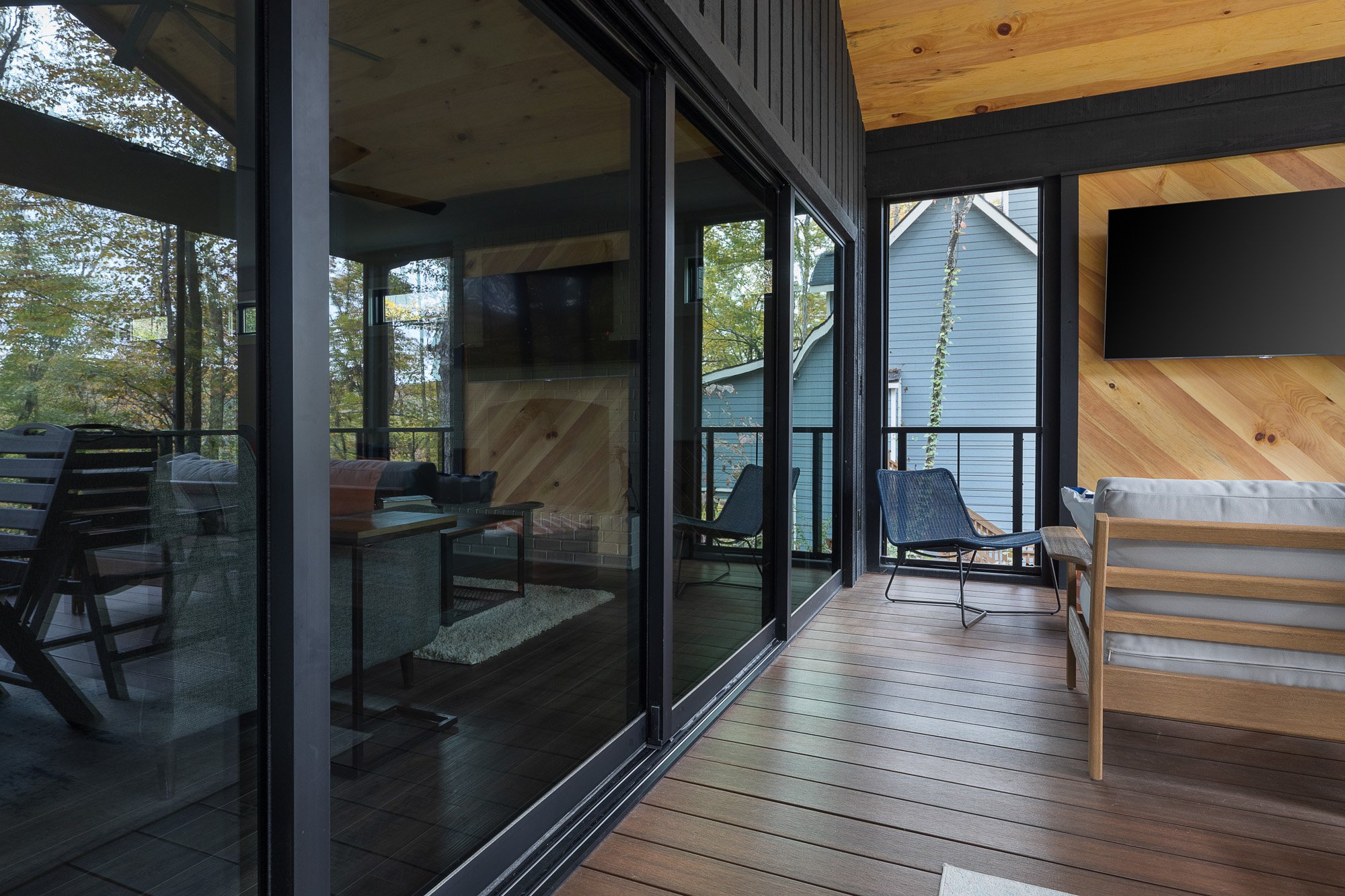 Screened-in porch with modern furniture and contrasting wood finishes, blending indoor and outdoor living.