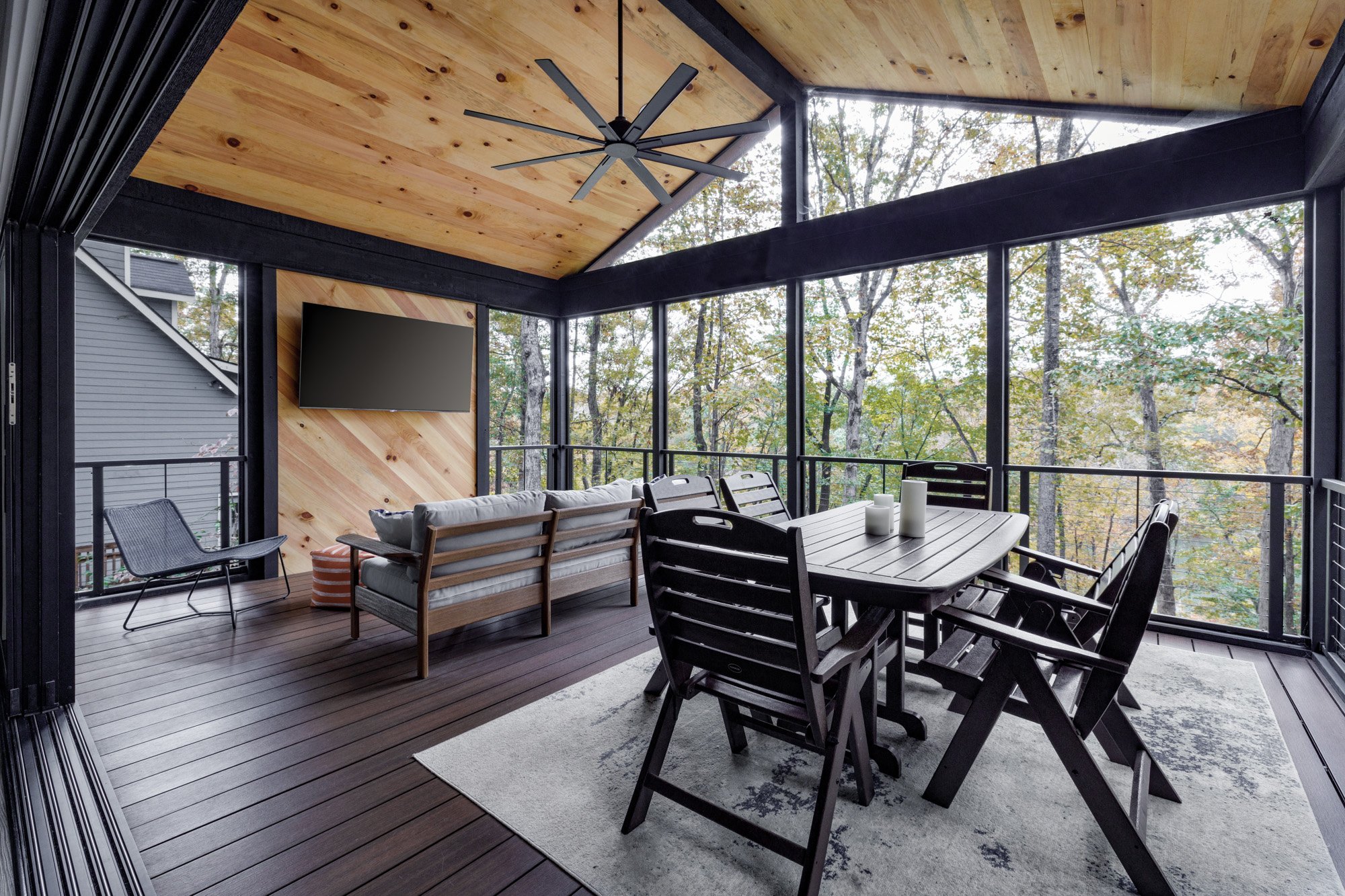 Modern enclosed porch with dining set, pine ceiling, and forest views through floor-to-ceiling windows.