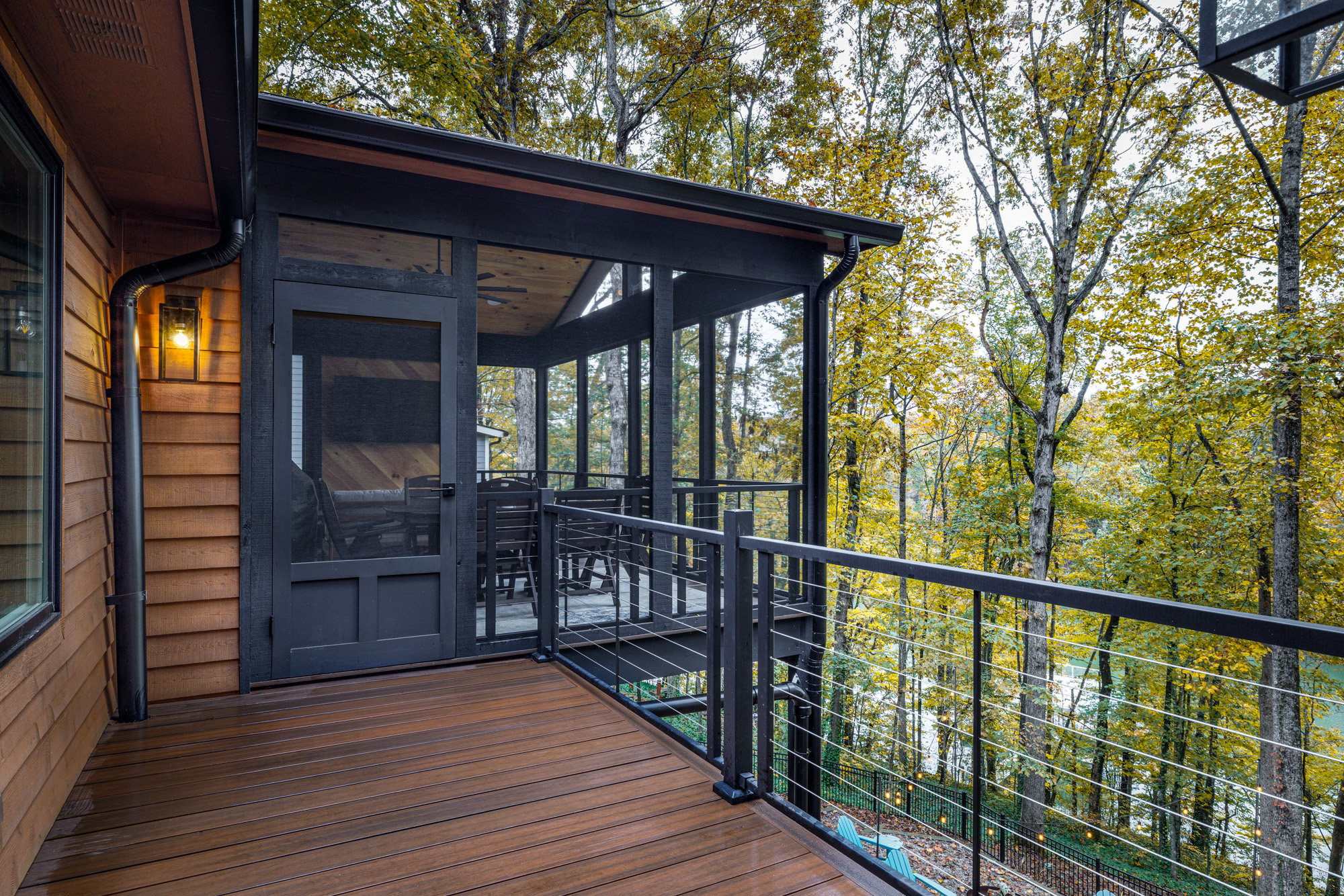 Wooden deck with screened porch area overlooking a serene forest in autumn.