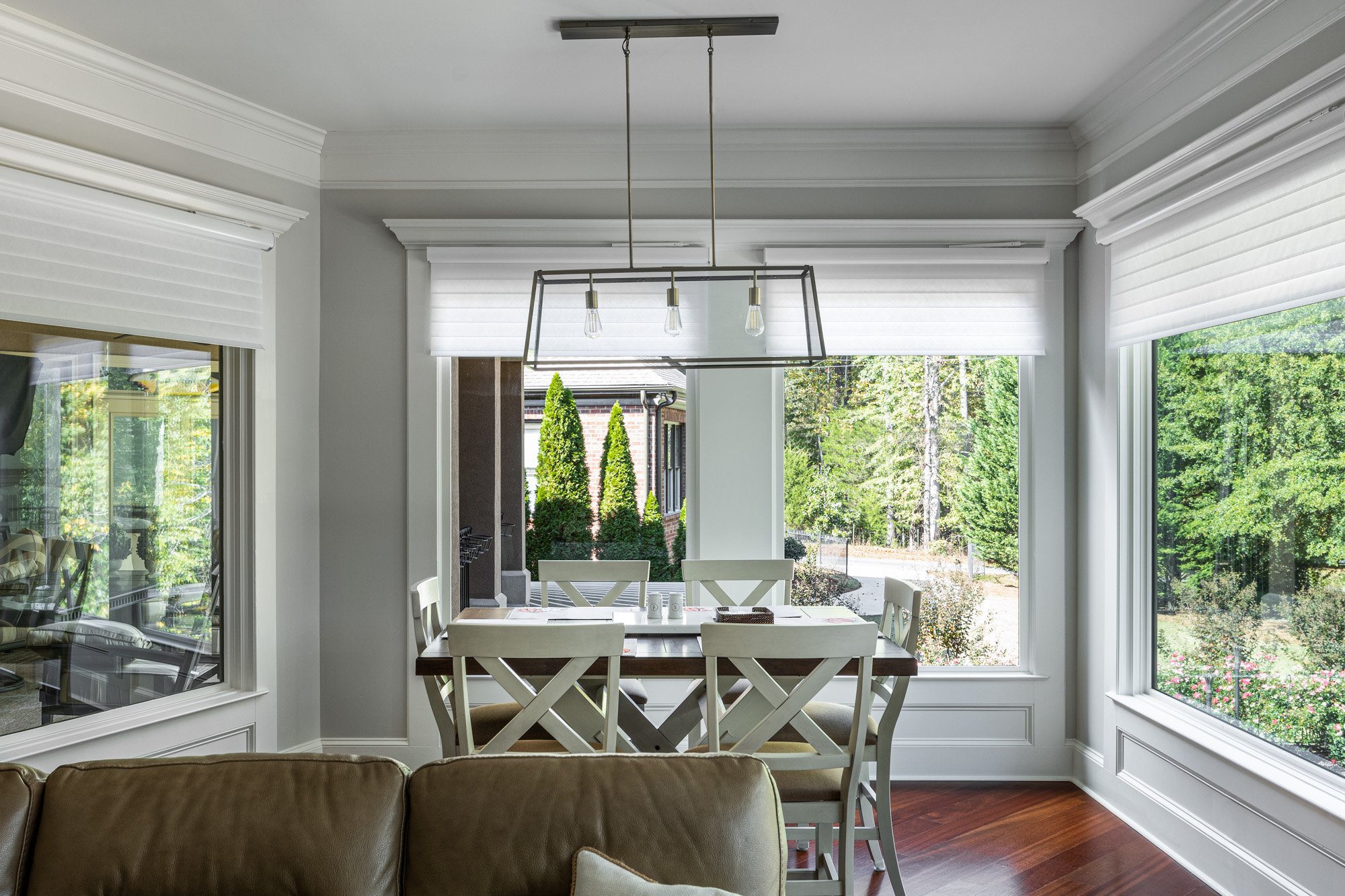 Elegant dining space with view to manicured garden through bay windows and a modern chandelier.