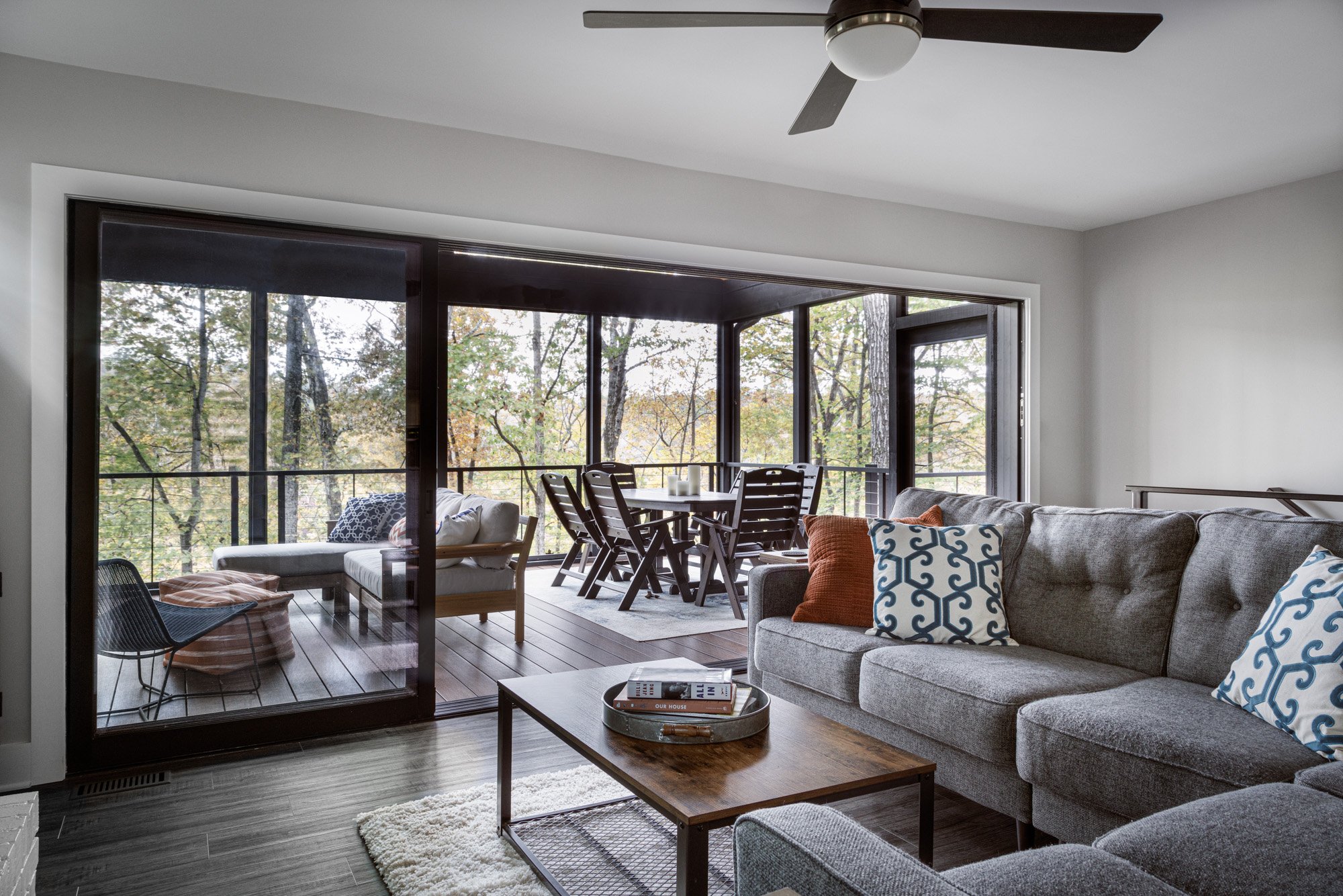 Stylish living room with large windows leading to a scenic deck surrounded by trees.