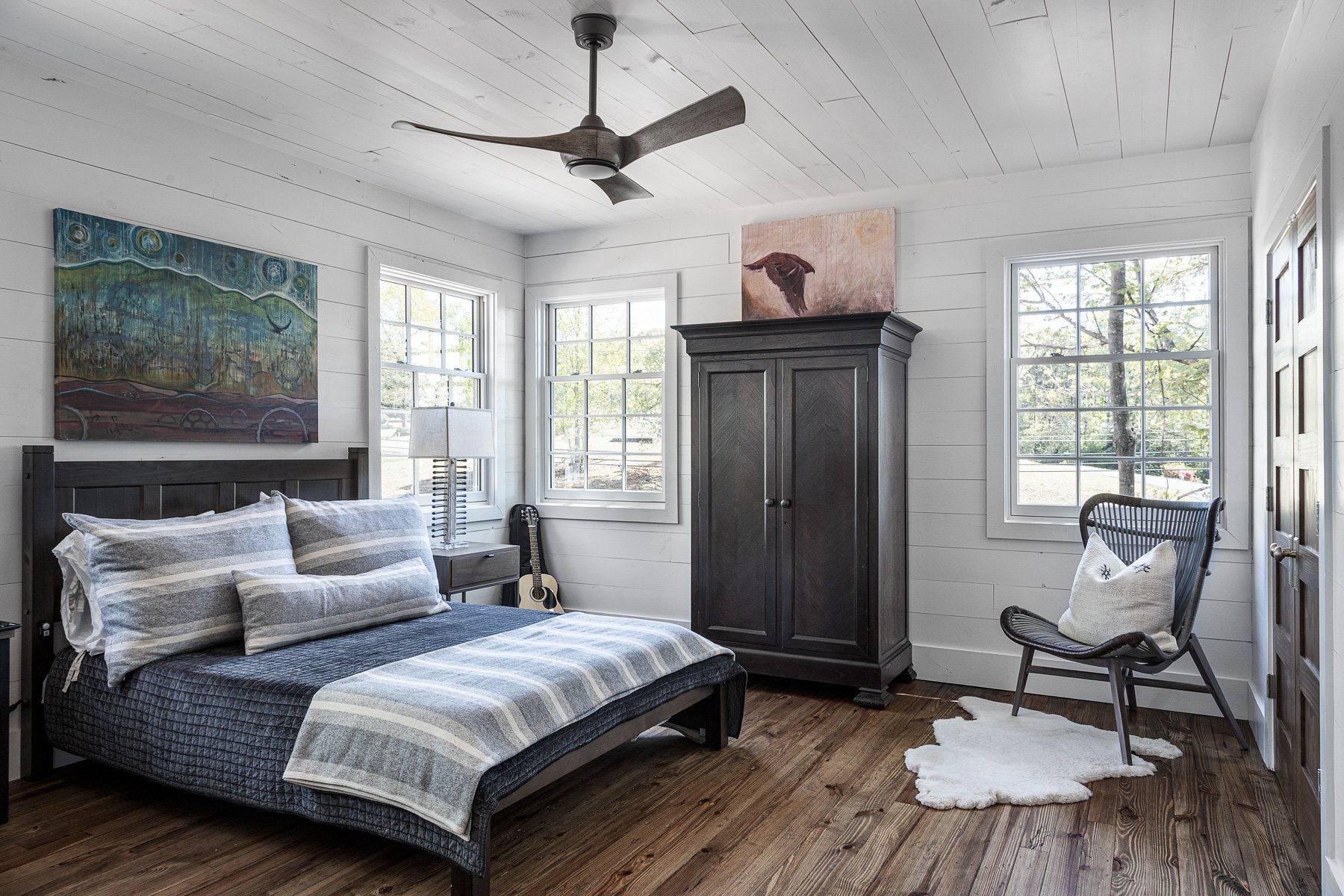 Spacious bedroom with artistic decor, hardwood floors, and a ceiling fan.